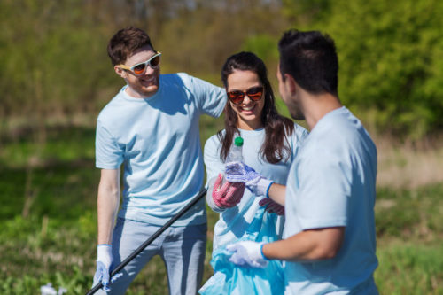 62354040 - volunteering, charity, cleaning, people and ecology concept - group of happy volunteers with garbage bags cleaning area in park